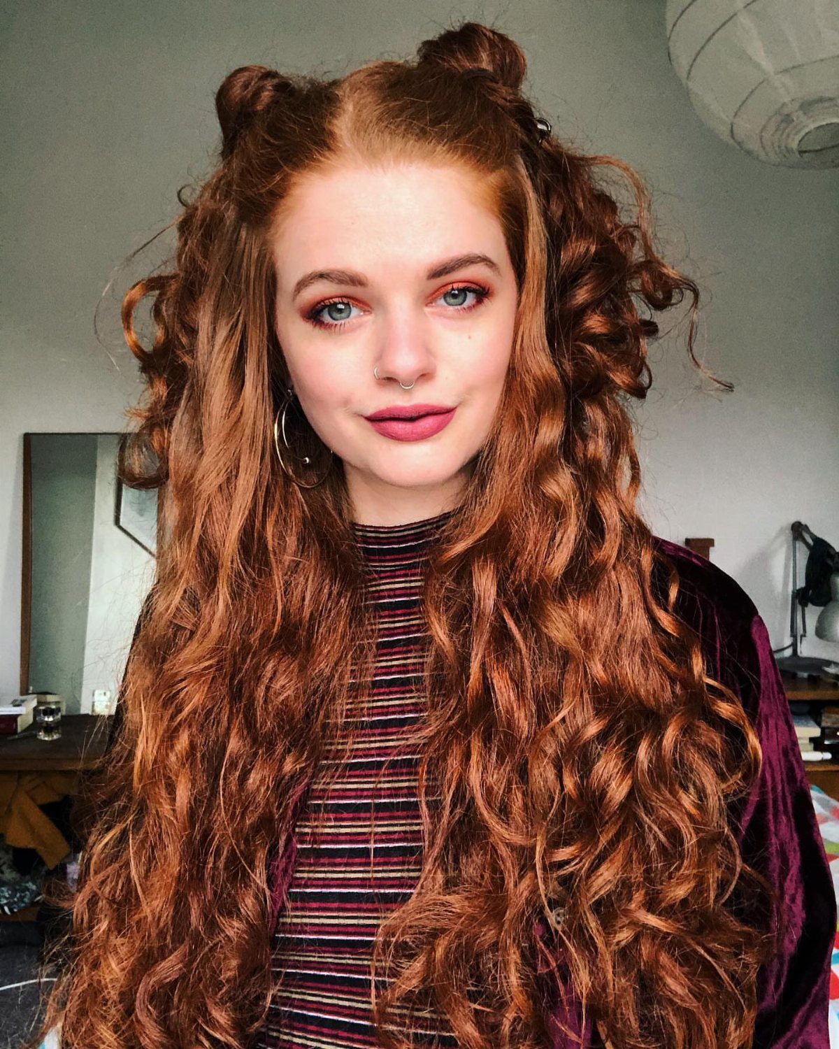 Woman with long auburn curls styled in two high space buns