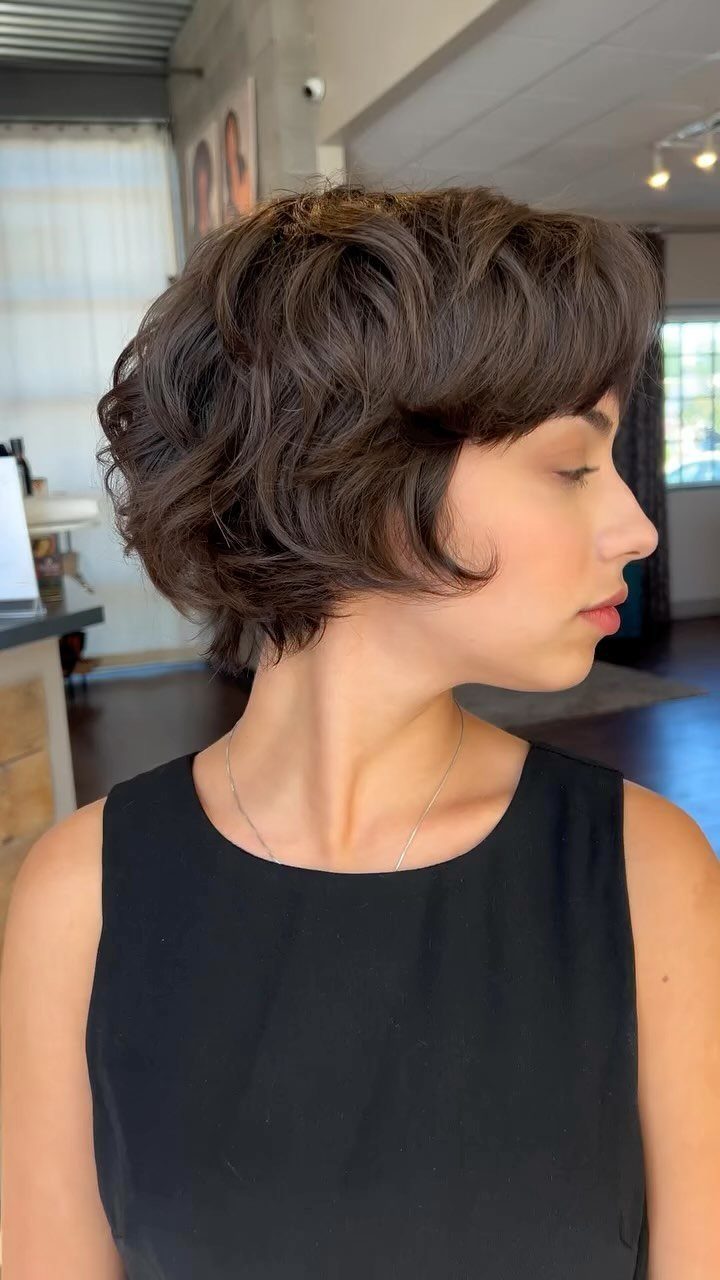 Woman with a voluminous dark brown wavy bixie haircut in a salon