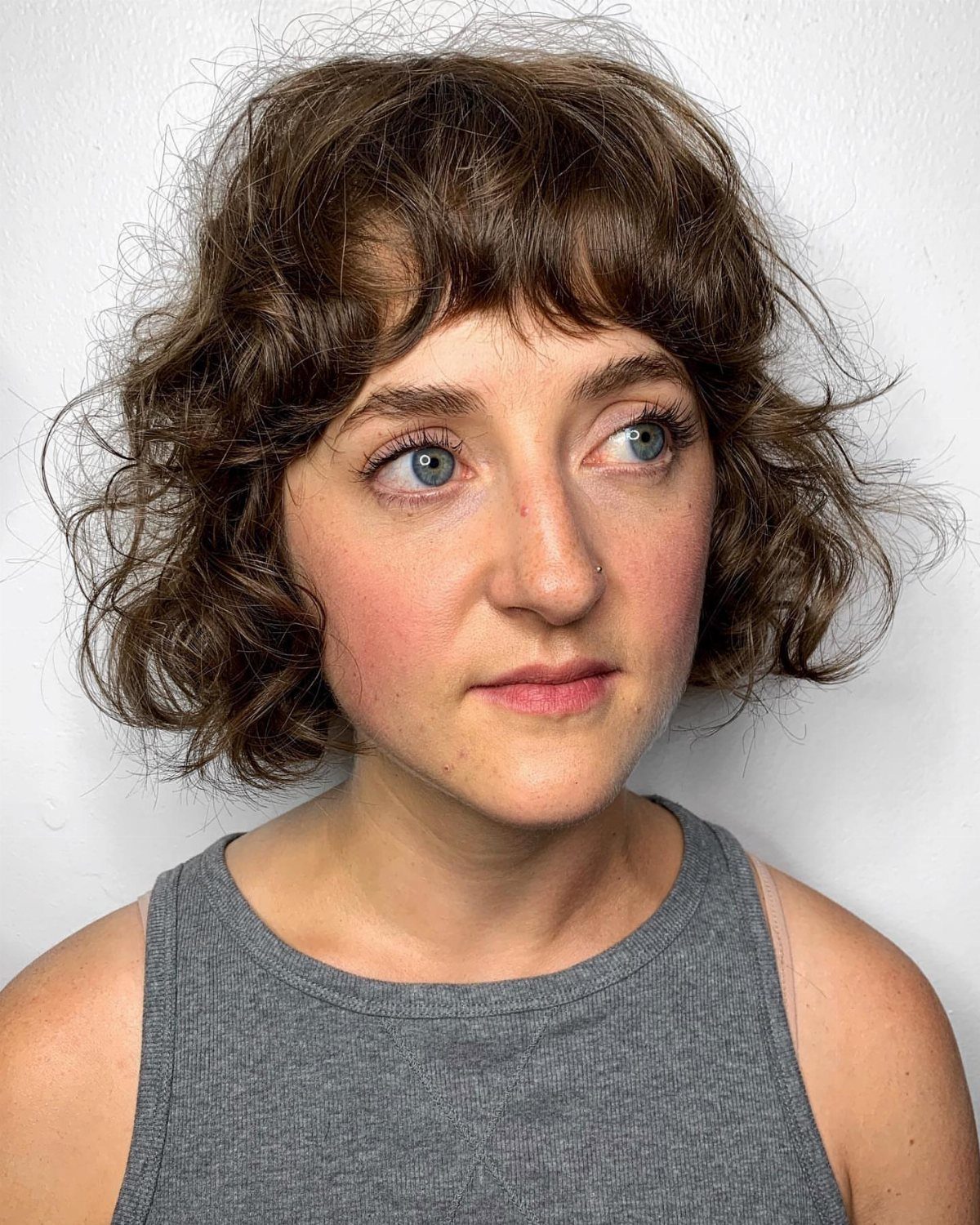 Woman showing short brown curls with a curly fringe and gray sleeveless top