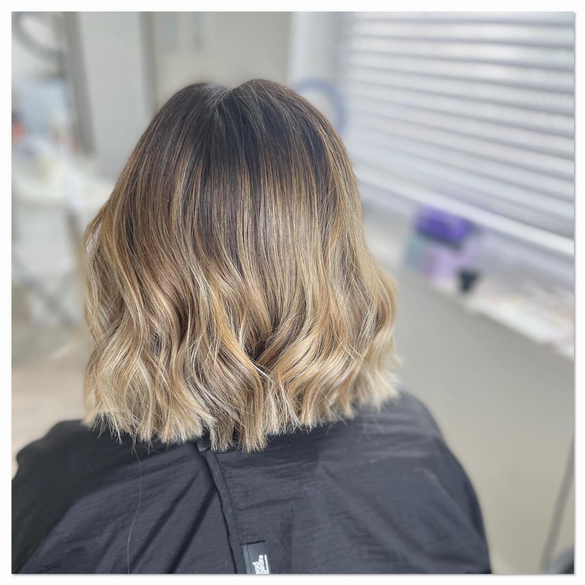 Shoulder-length wavy bob with dark roots fading into blonde ends