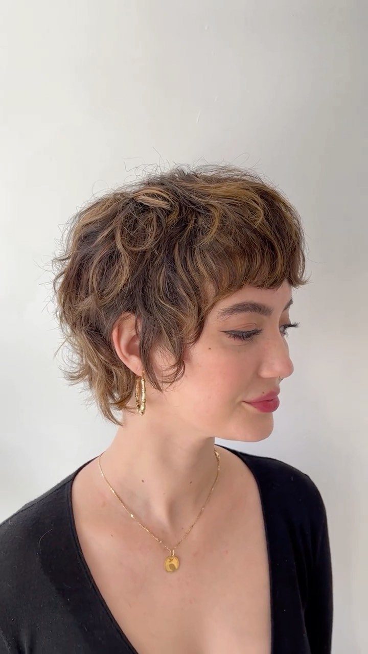 Woman with tousled brown curly mullet, shorter sides and longer back