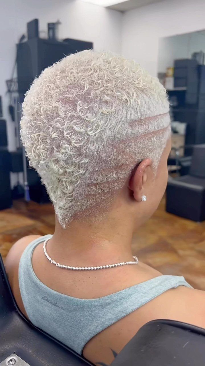 Short platinum curls contrast with a shaved, line-patterned undercut at the salon