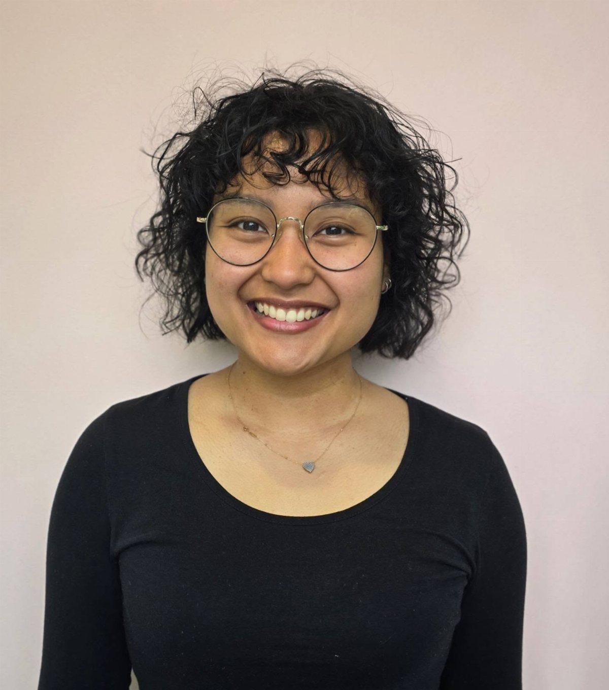Short defined curls frame a smiling person's face above a black top.