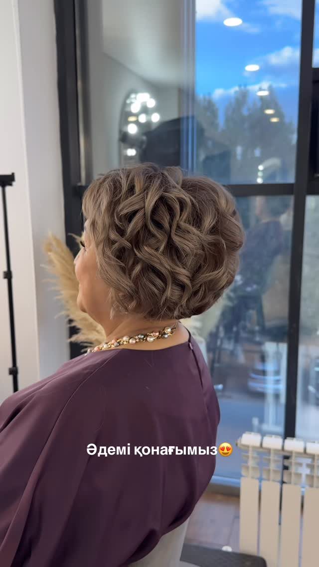 Woman showing a short, curled updo while seated in a salon chair