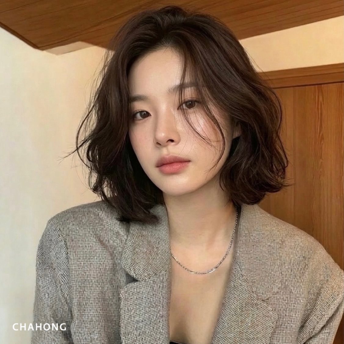 Woman with a short, softly wavy dark bob wearing a gray tweed jacket