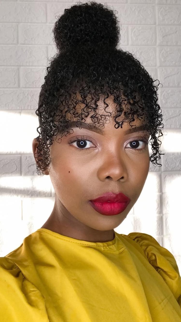 Woman with a high curly bun, forehead bangs, and short tapered sides