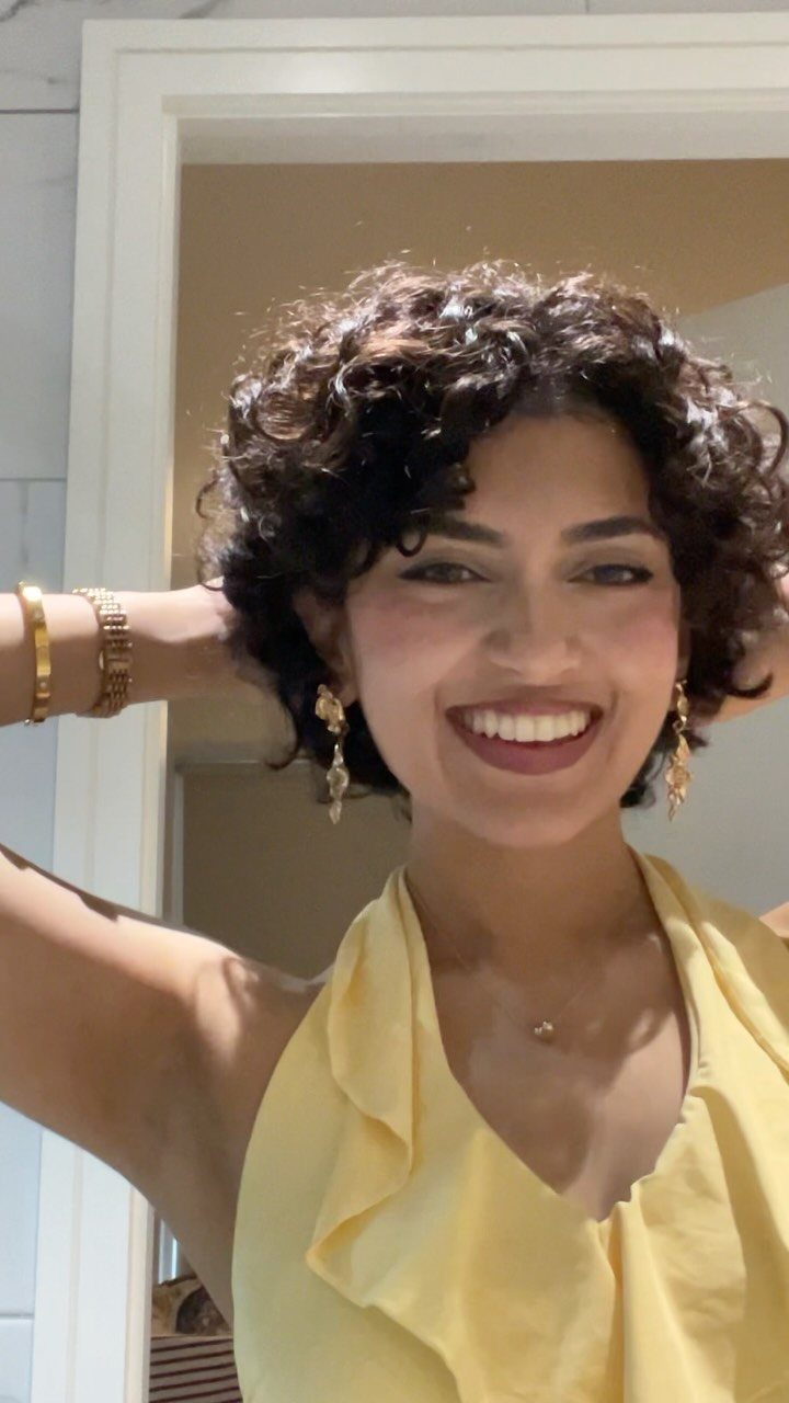 Smiling woman showcasing short curly dark hair in a yellow sleeveless top