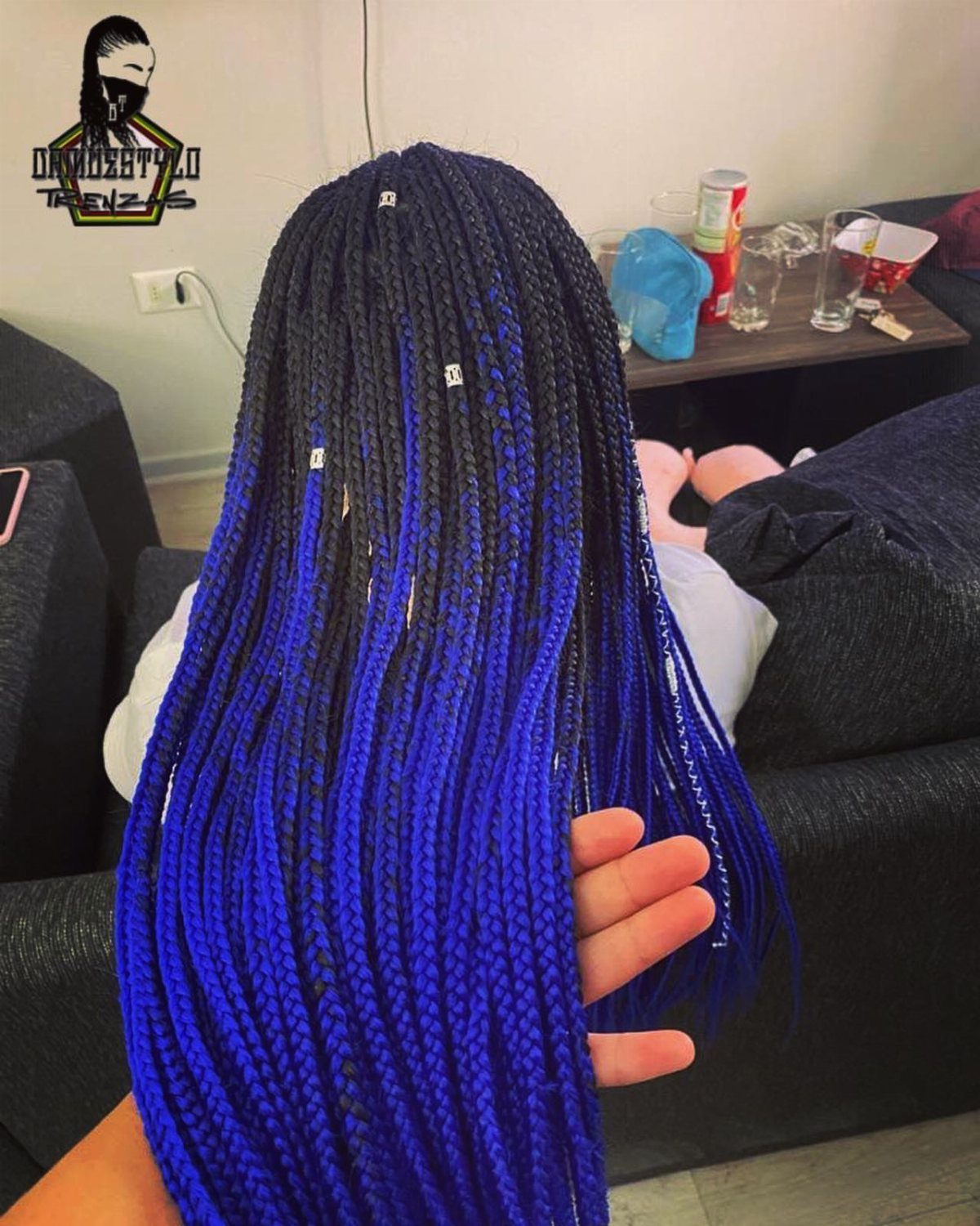 Long black braids transition to vivid blue ends, displayed by a hand in a salon.