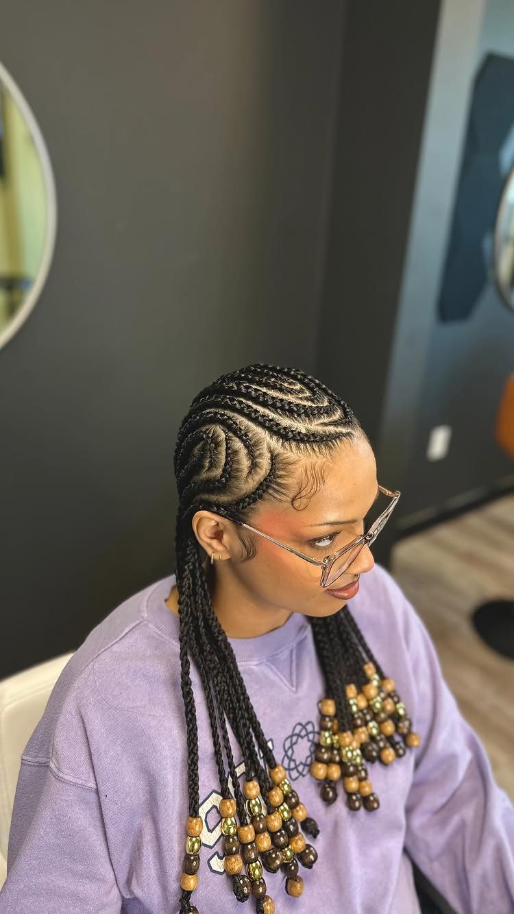 Long cornrow braids decorated with gold and brown beads hang over a lavender top