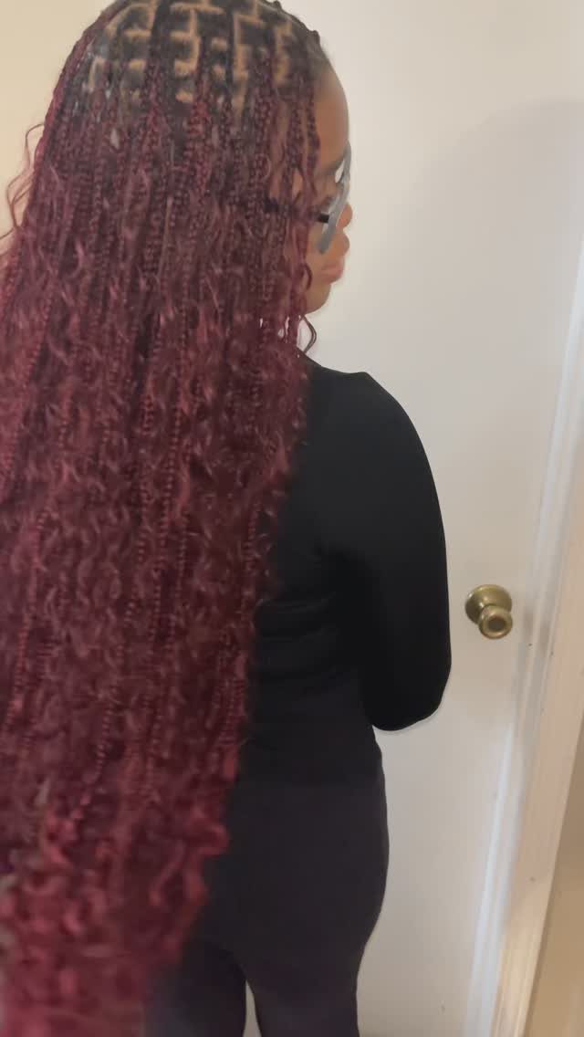 Long burgundy braids with curly texture fall down a person’s back