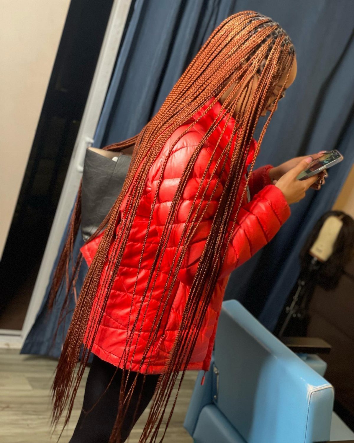 Long copper-orange braids cascade down the back of a person in a red jacket