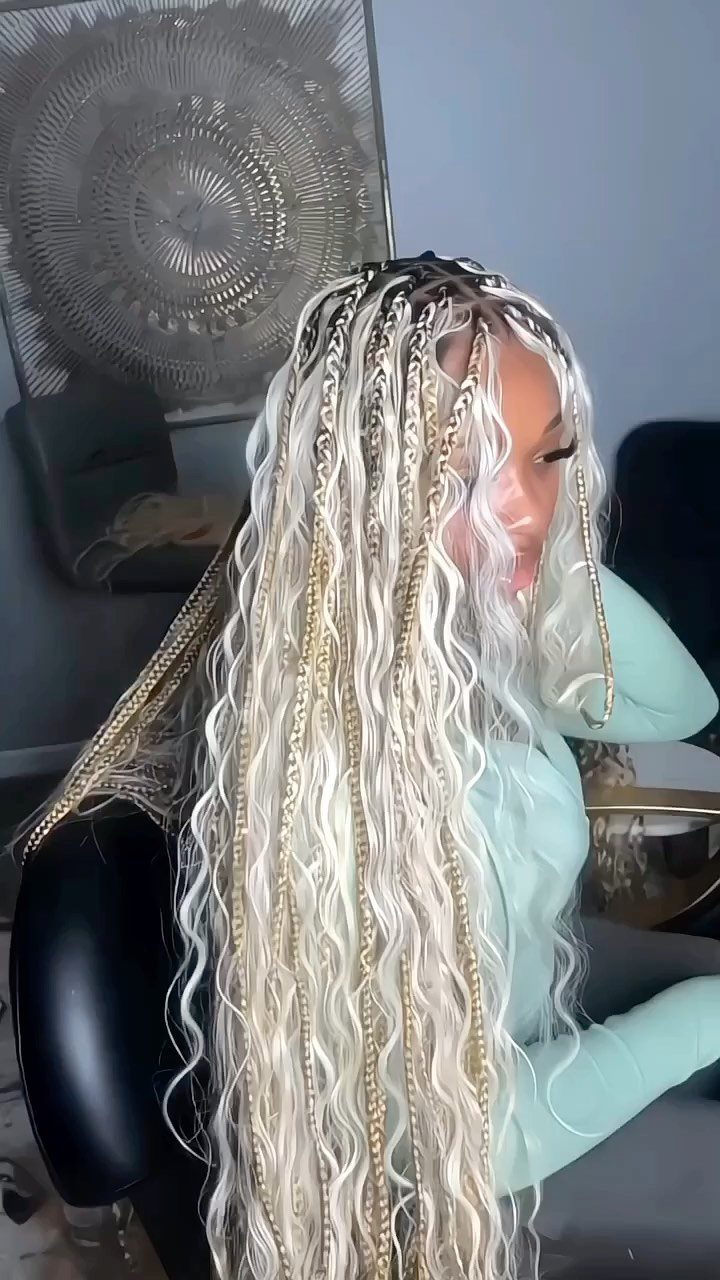 Long pale blonde braids mixed with loose wavy strands drape over a seated person