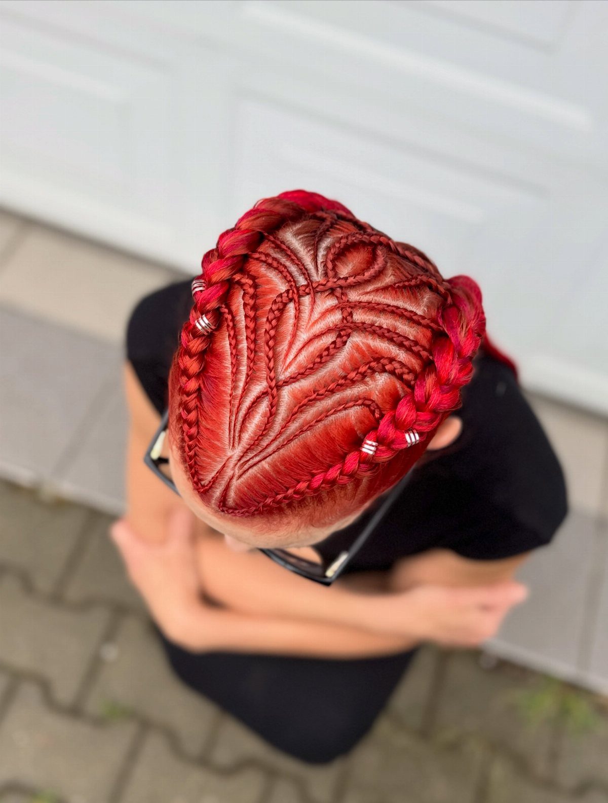 Red cornrows curve into heart-like patterns across the person's scalp