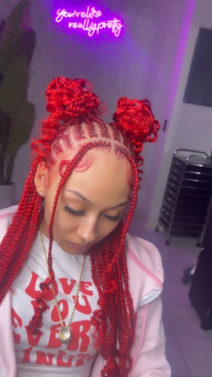 Bright red braids styled into curly buns and long lengths on a seated person