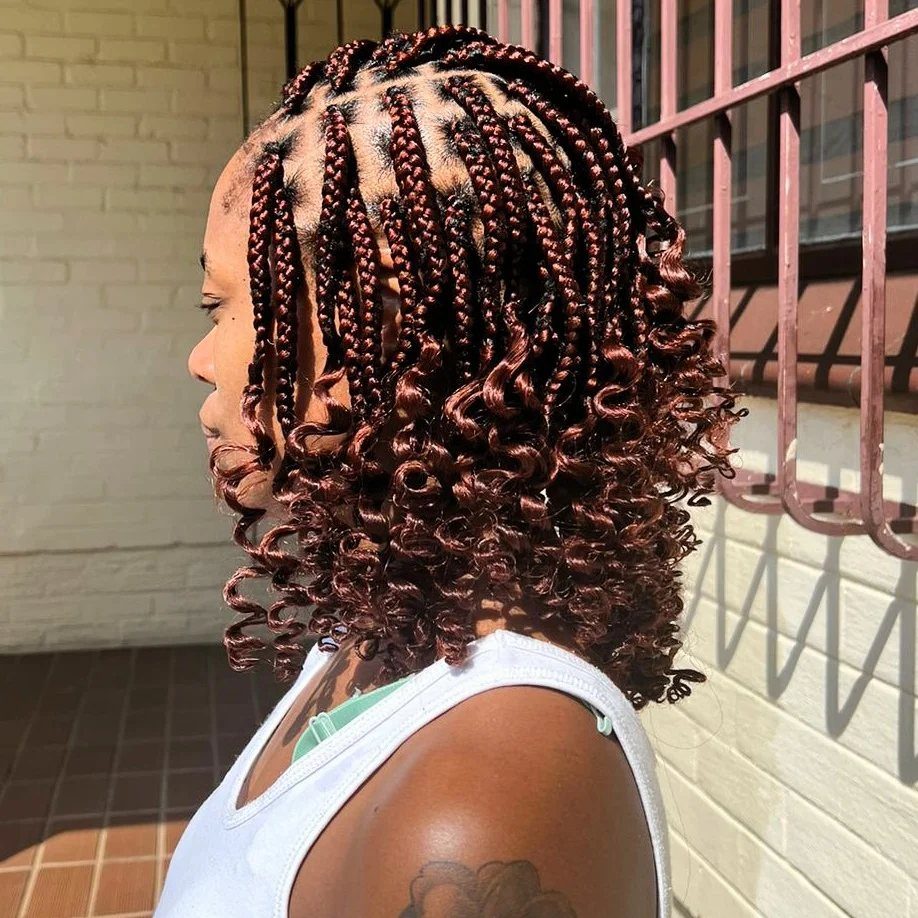 Short burgundy box braids end in curls on a person outdoors