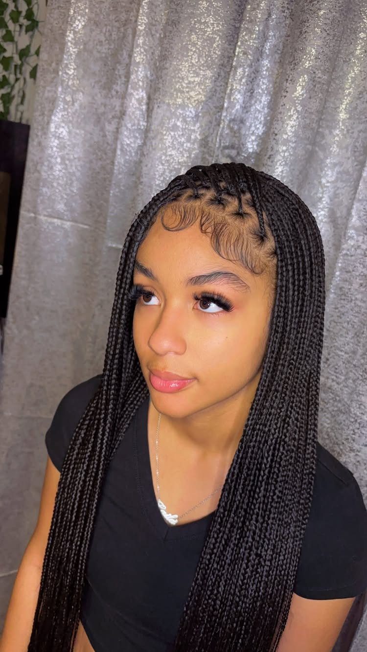 Woman with long, thin black box braids and styled baby hairs in front of a curtain