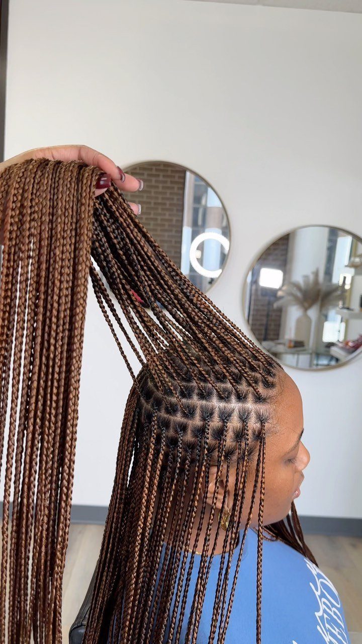 Long brown box braids held overhead cascade past the shoulders