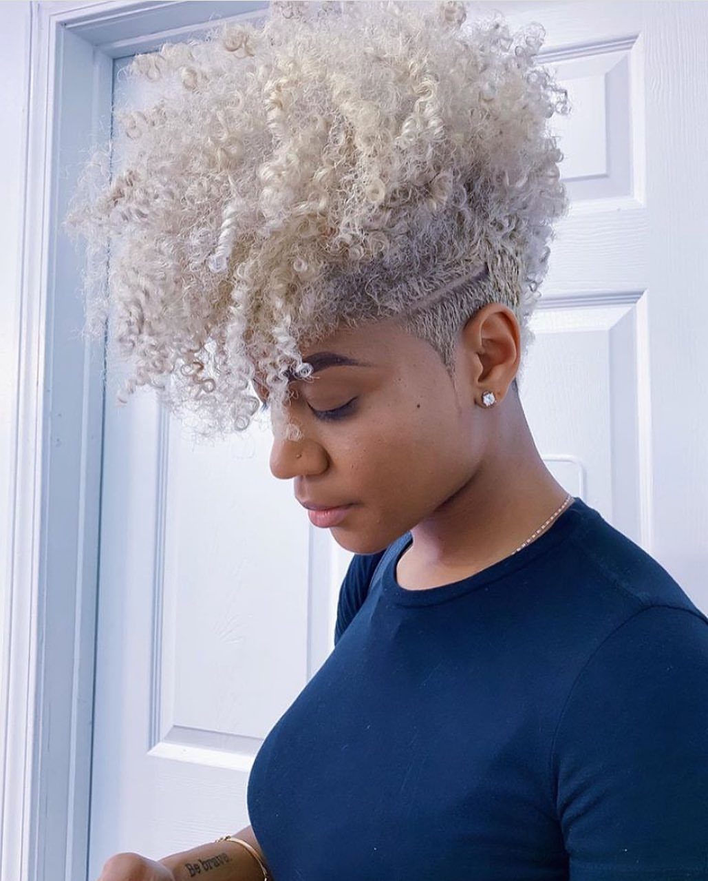 Short blonde curly afro with pale highlights frames a person's face