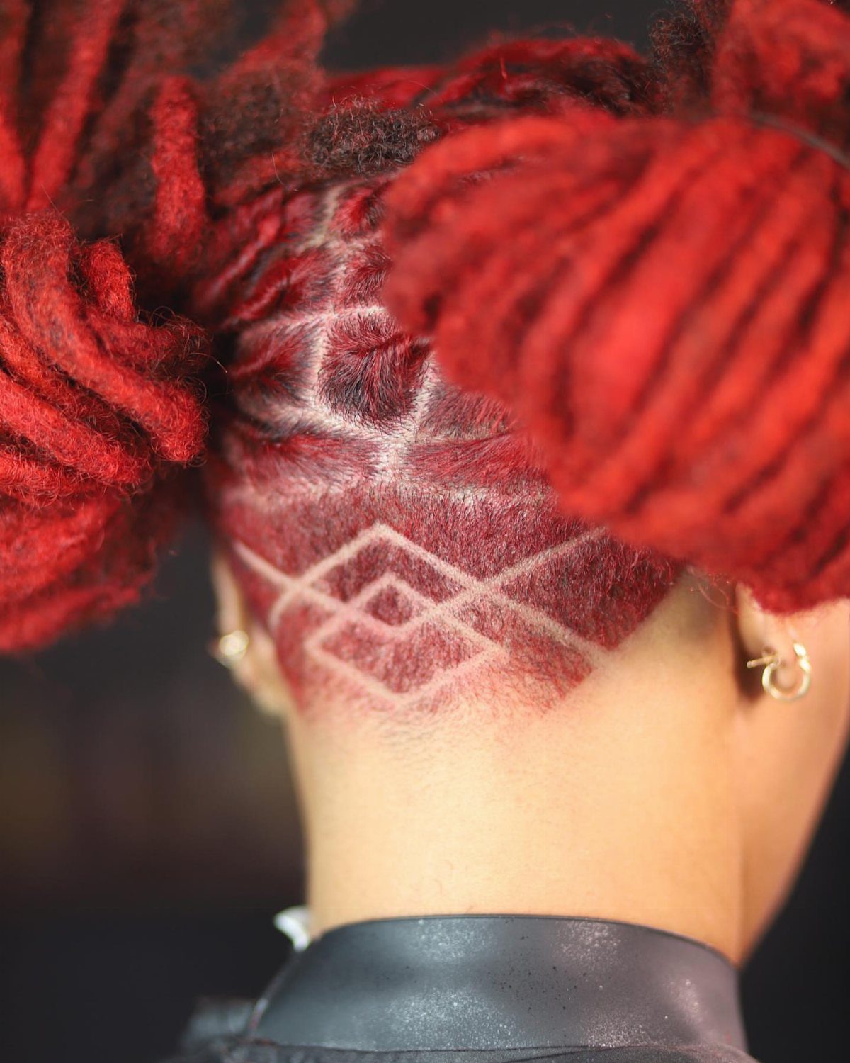 Red locs reveal a shaved side with geometric hair designs and a hoop earring