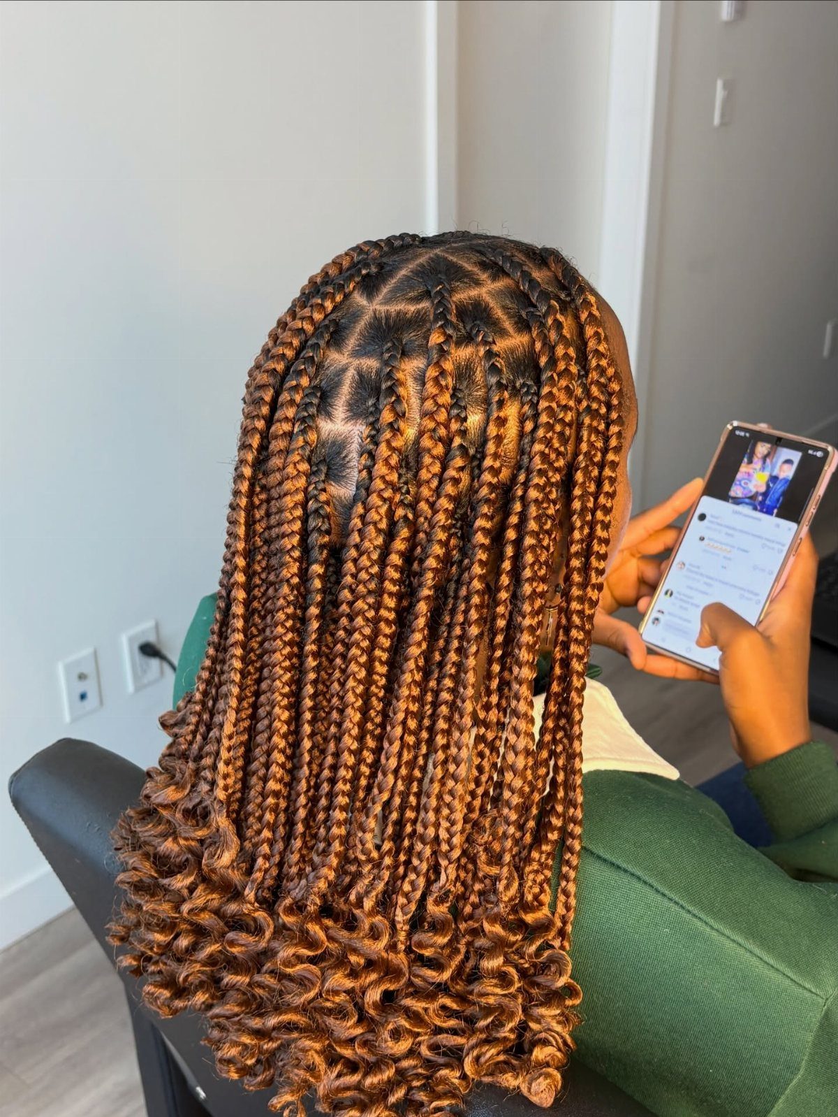Small brown and black braids with curled ends fall down a seated person's back