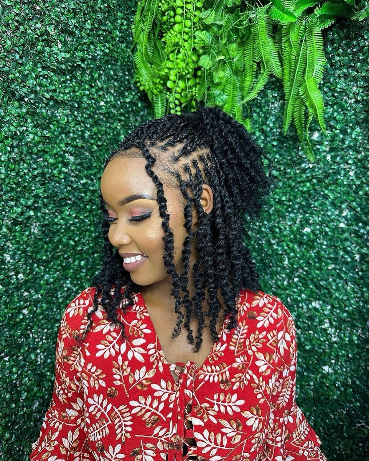 Woman wearing long black twists gathered loosely at the back against a leafy green wall
