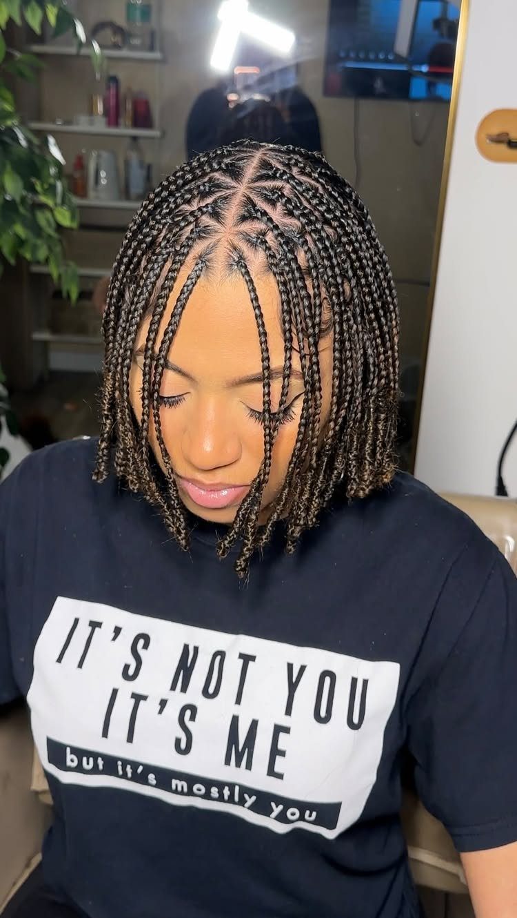 Short black box braids with triangular scalp parts frame a person's face
