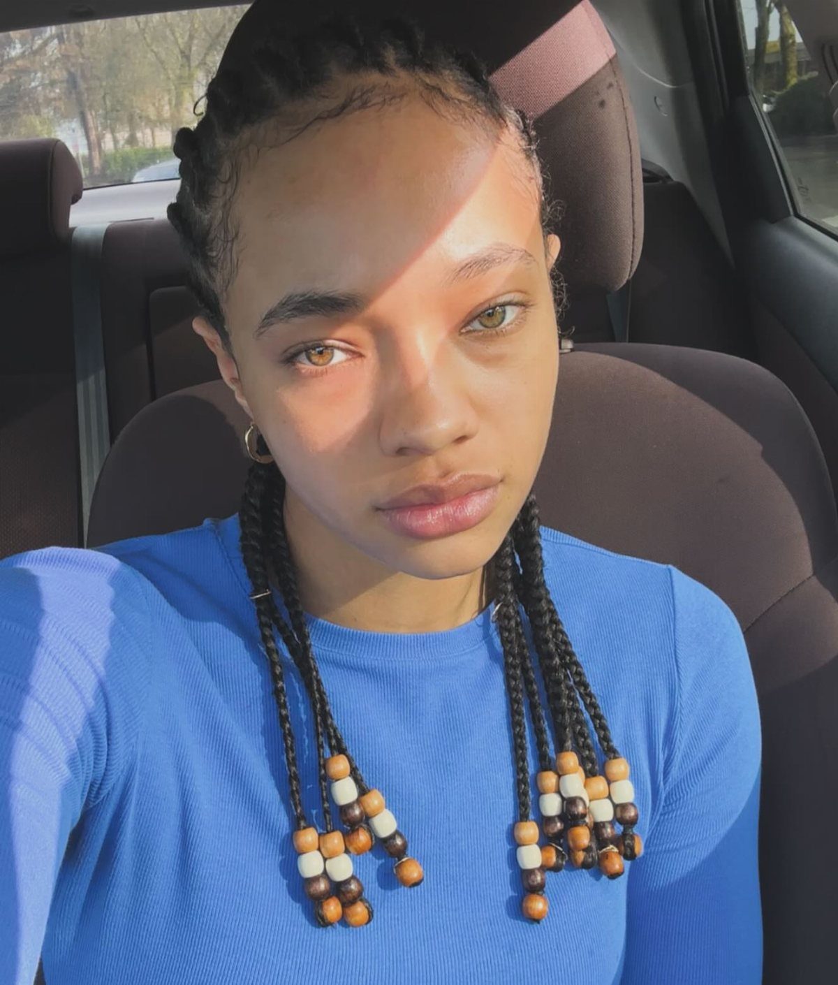 Woman wearing long beaded twists with the upper hair pulled back in a car