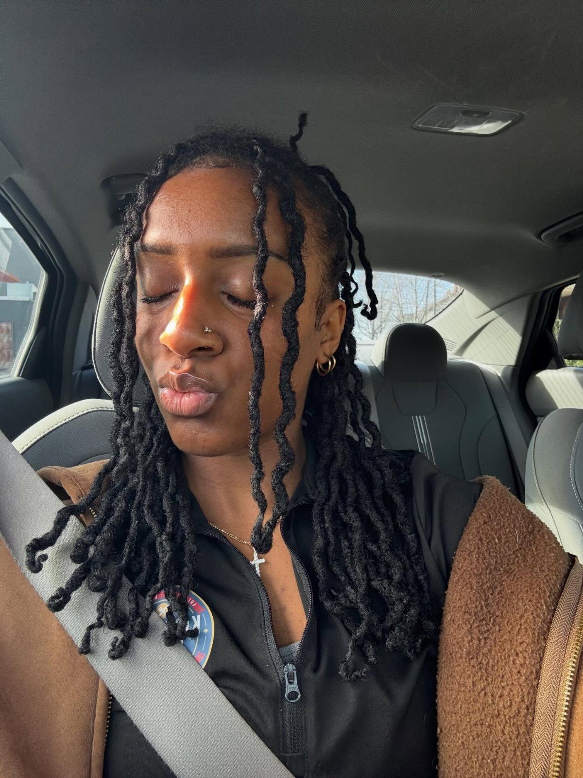Long thick black twists frame a person seated in a car
