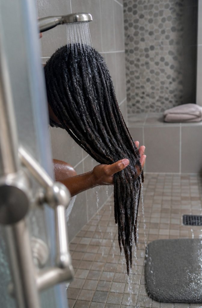 Dark locs gently squeezed under clear water as white lather rinses away