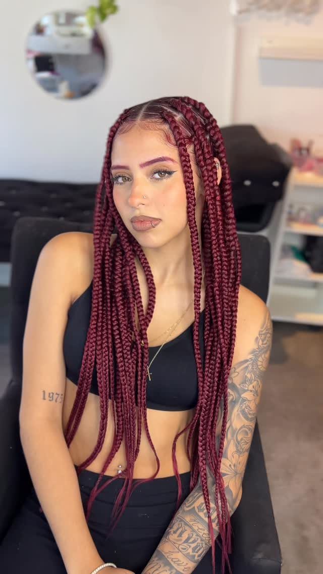 Woman displaying long burgundy jumbo box braids while seated indoors