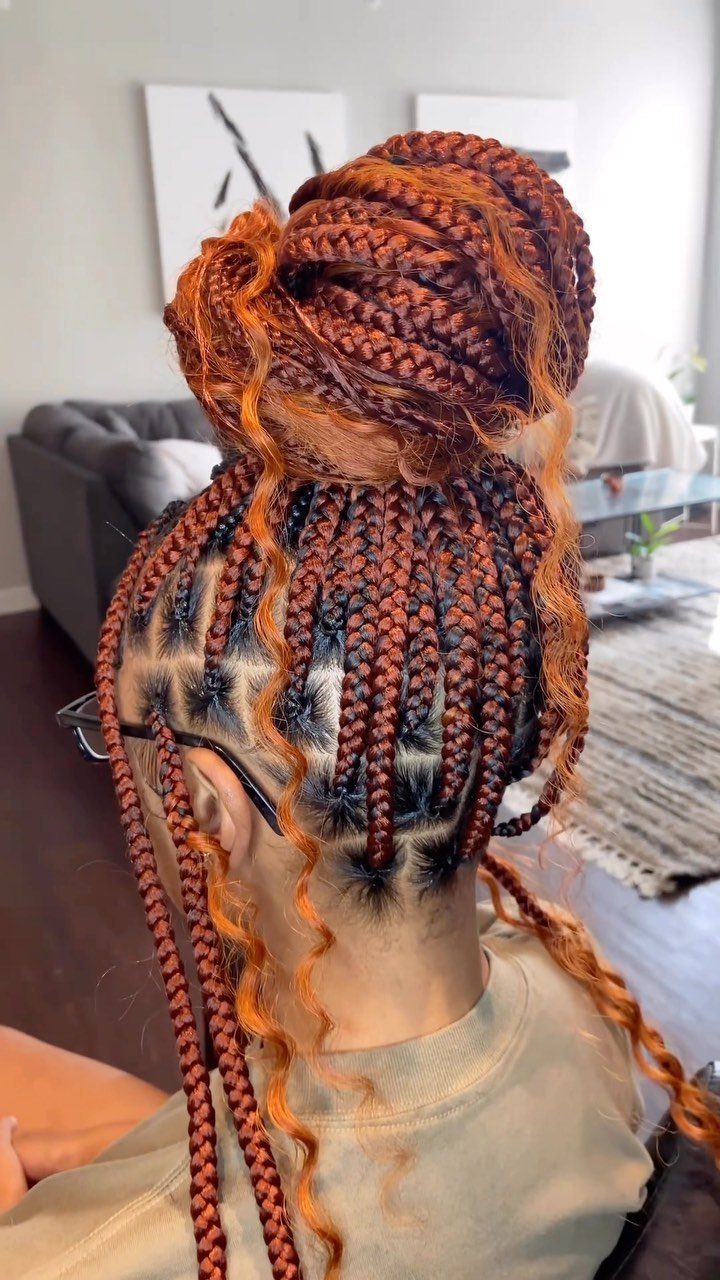 Copper and dark jumbo box braids gathered in a bun with curled ends