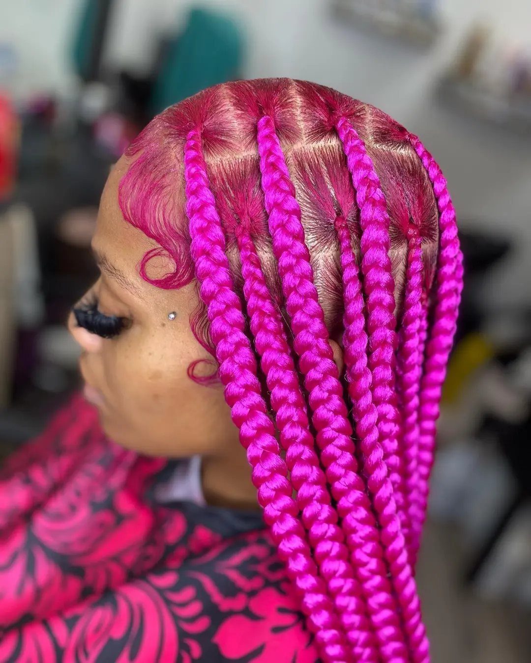 Bright fuchsia braids fall over a person's shoulder above pink patterned clothing