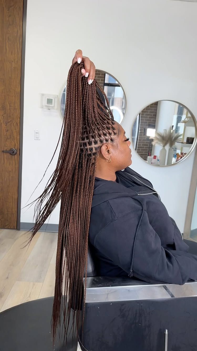 Woman holds long glossy brown jumbo box braids in a salon chair