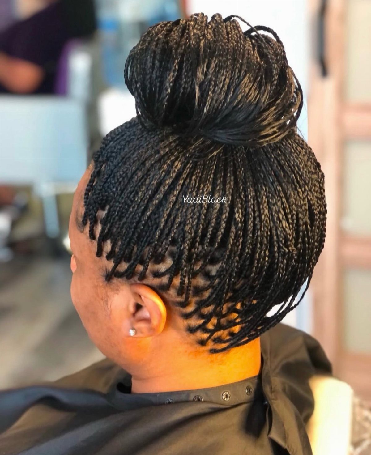 Dark box braids gathered into a large high bun at a salon
