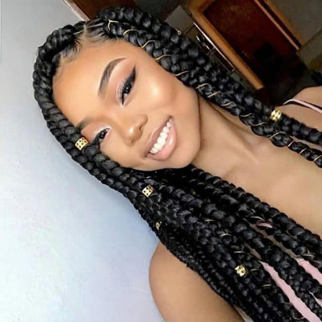 Woman smiles with long black box braids decorated with small gold cuffs