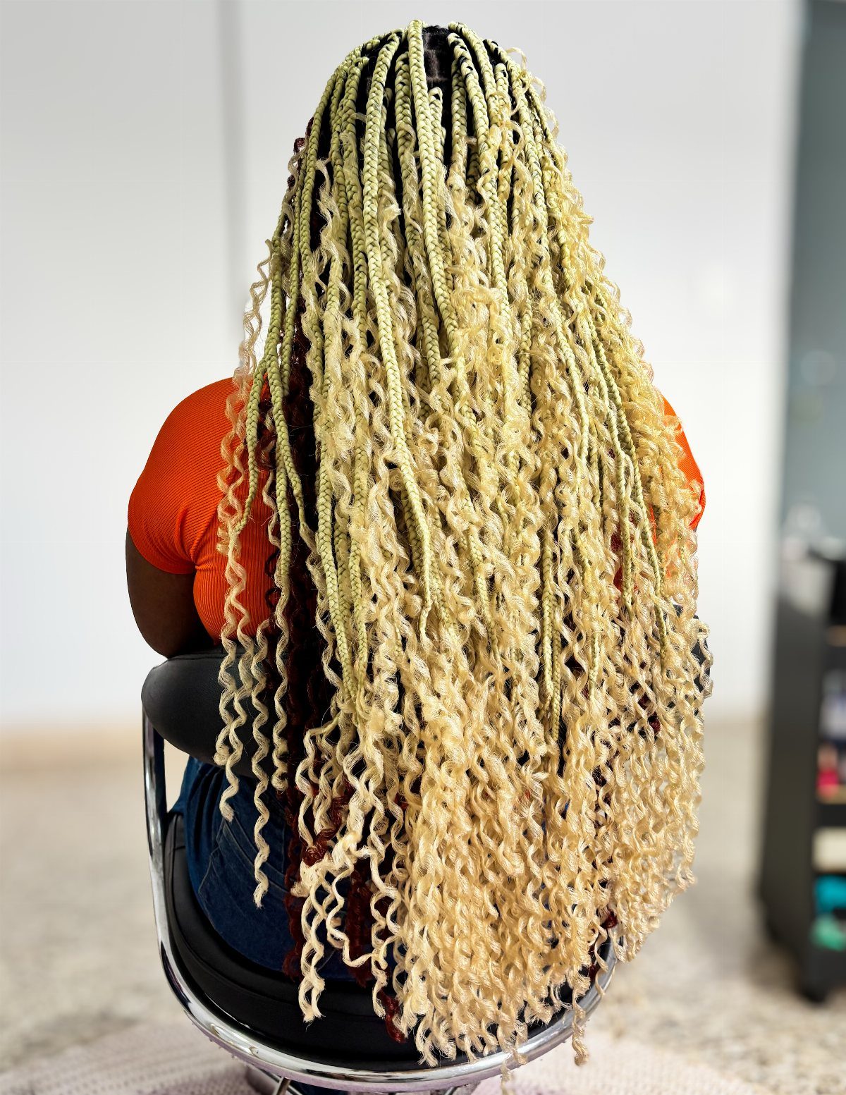 Long blonde goddess braids with curly ends cascade down a seated person's back