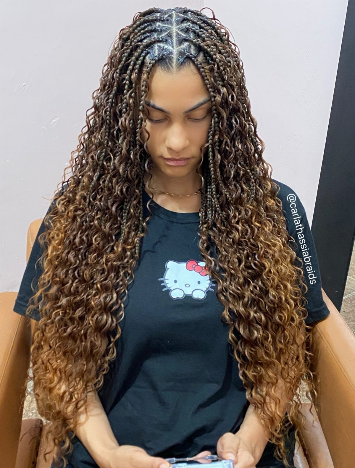 Long dark-rooted braids fading to light brown curly lengths frame a seated person