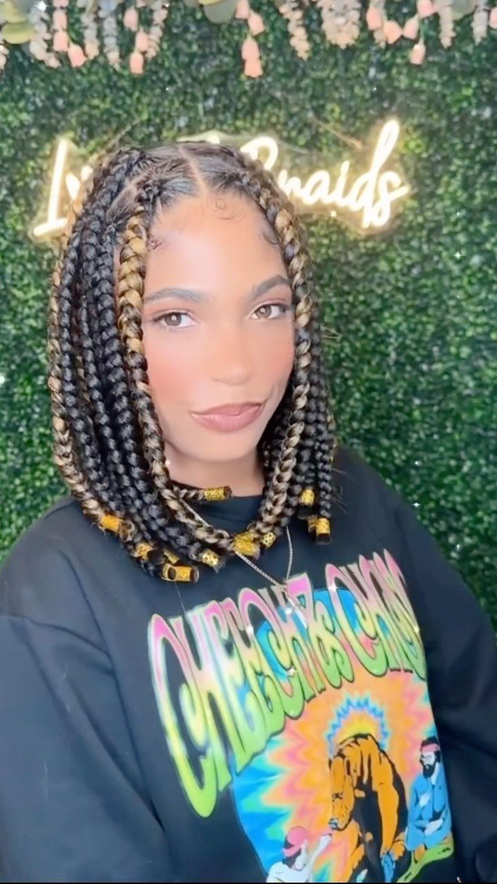 Shoulder-length black jumbo box braids with gold cuffs frame a person’s face