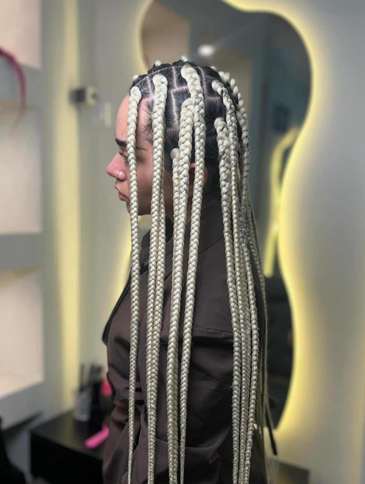Long silver-gray jumbo box braids cascade down a person's back in a salon