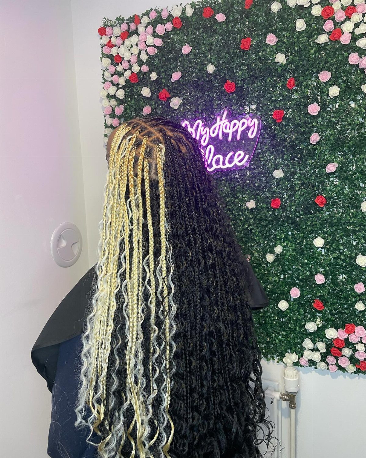 Long black braids with a broad blonde streak against a flower-covered wall