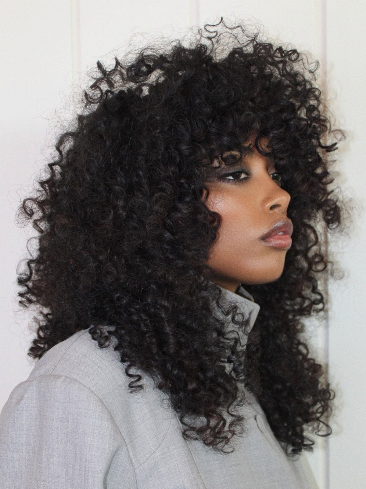 Voluminous dark curls form a rounded layered shape around the person's face