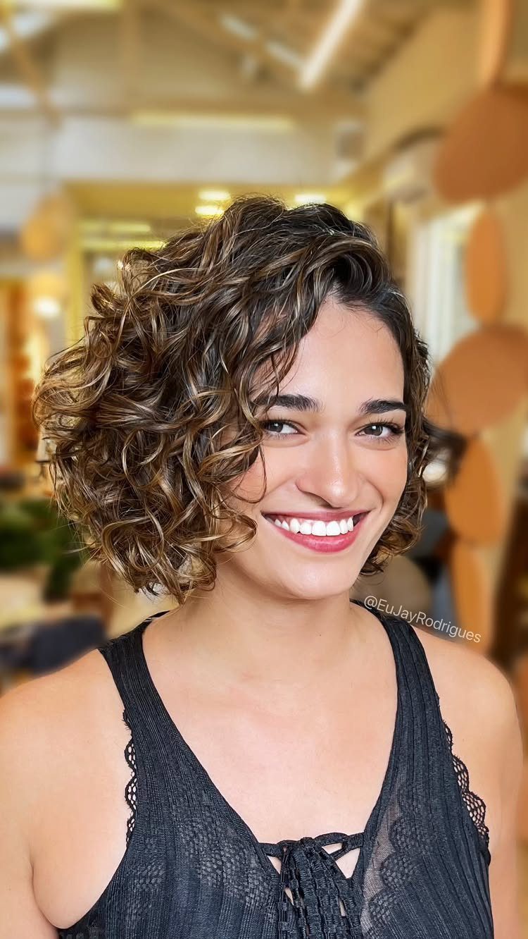 Woman showing a rounded, layered curly bob with dark shoulder-grazing curls