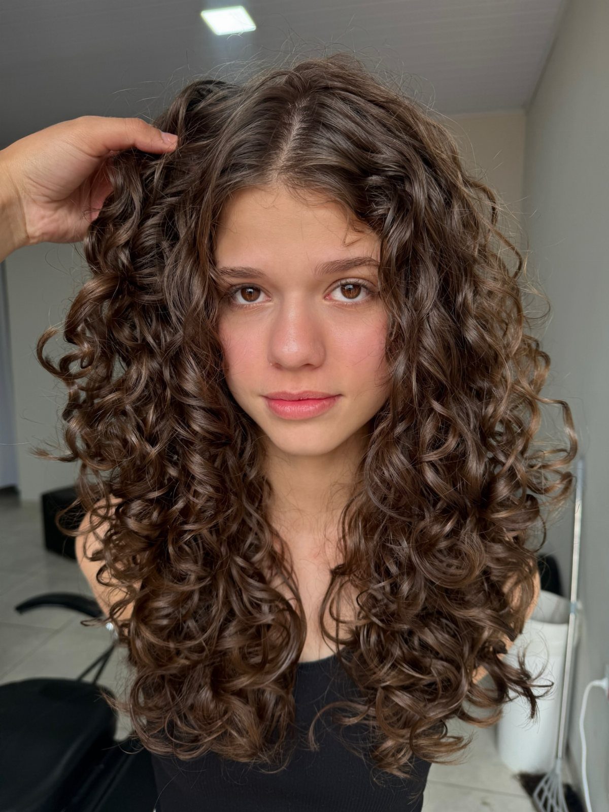 Woman with voluminous long brown curls, with a hand lifting hair near her crown