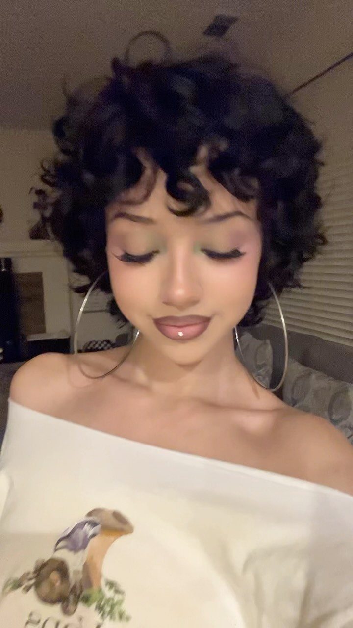 Person showcasing a short, voluminous curly TWA hairstyle with defined bangs