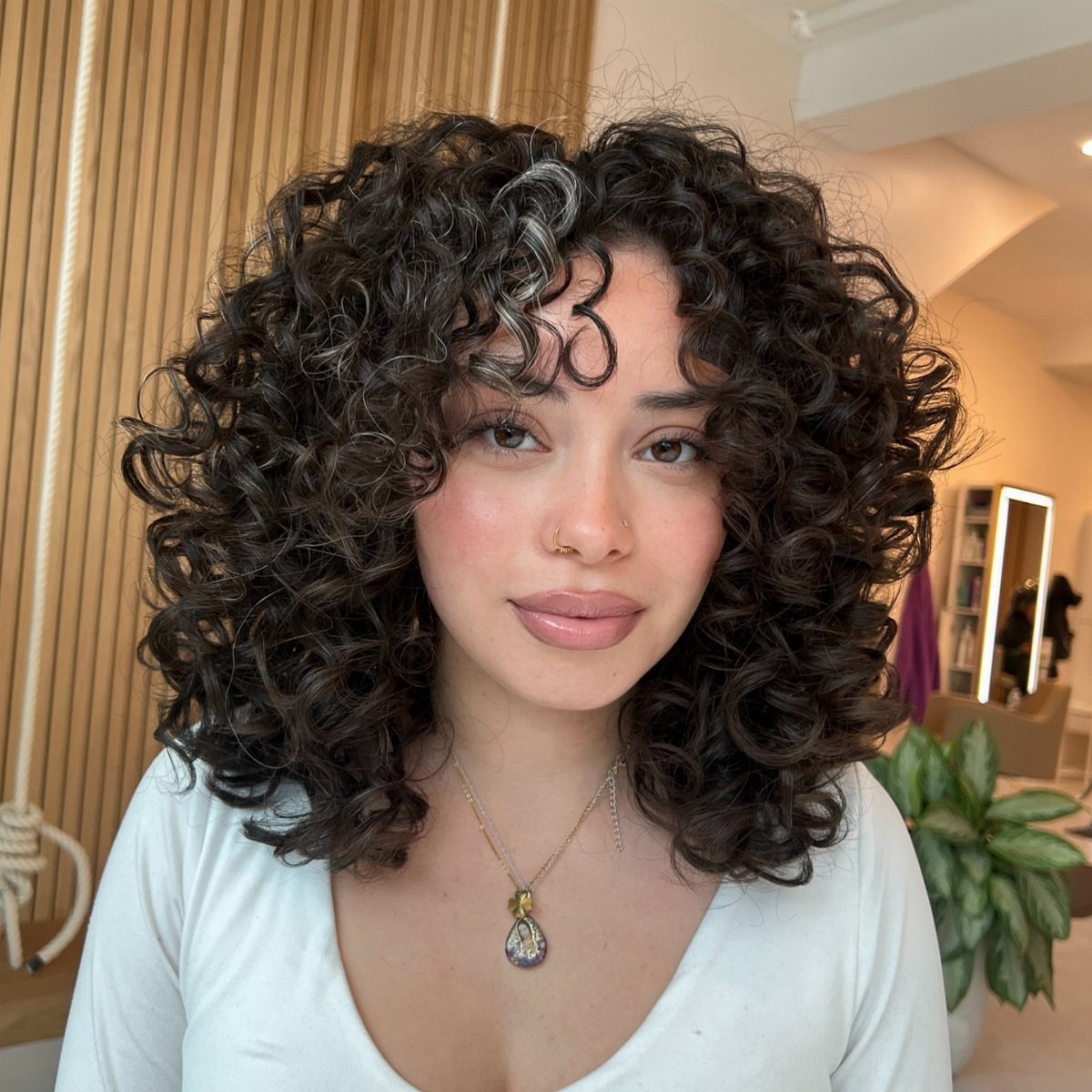 Person with voluminous shoulder-length dark curls and soft, layered ends