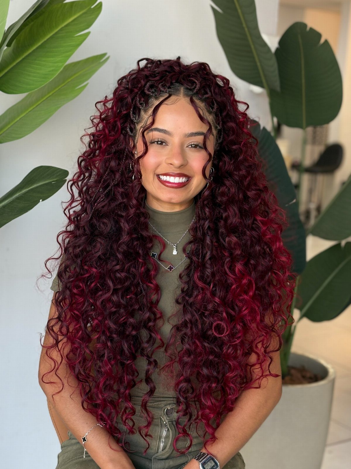 Woman with long, voluminous burgundy curls sitting among broad green leaves