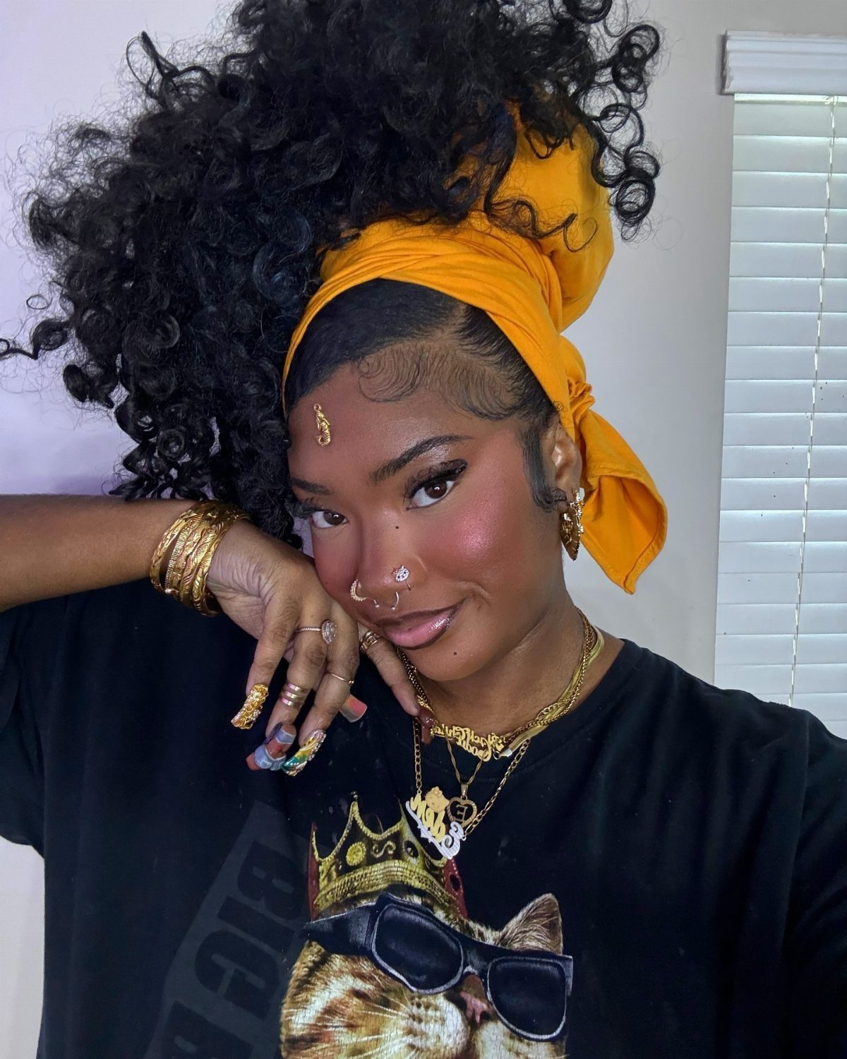 Woman wearing high gathered curls with an orange head wrap and gold jewelry