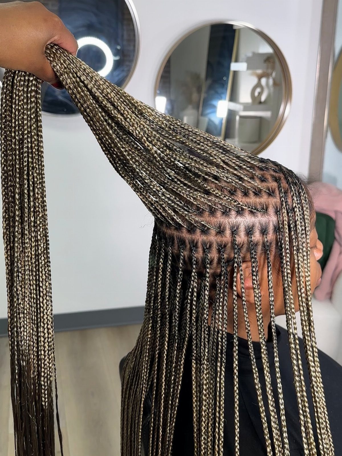 Ash-blonde box braids reveal dark roots in a close-up salon styling view