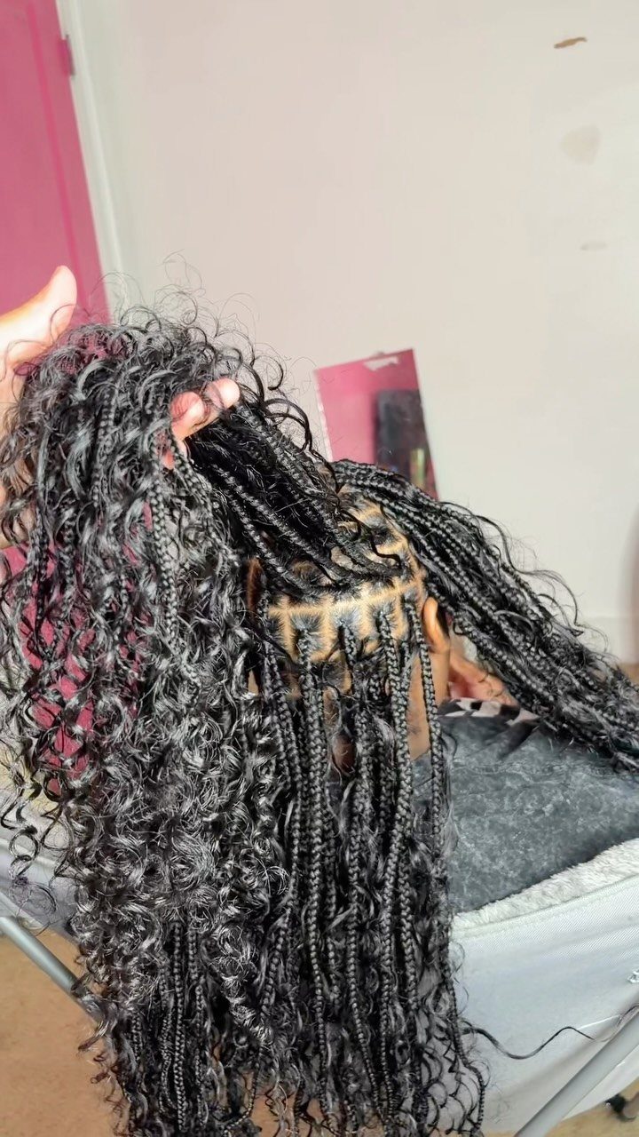 Black box braids with loose curls hang over the client's head in a salon