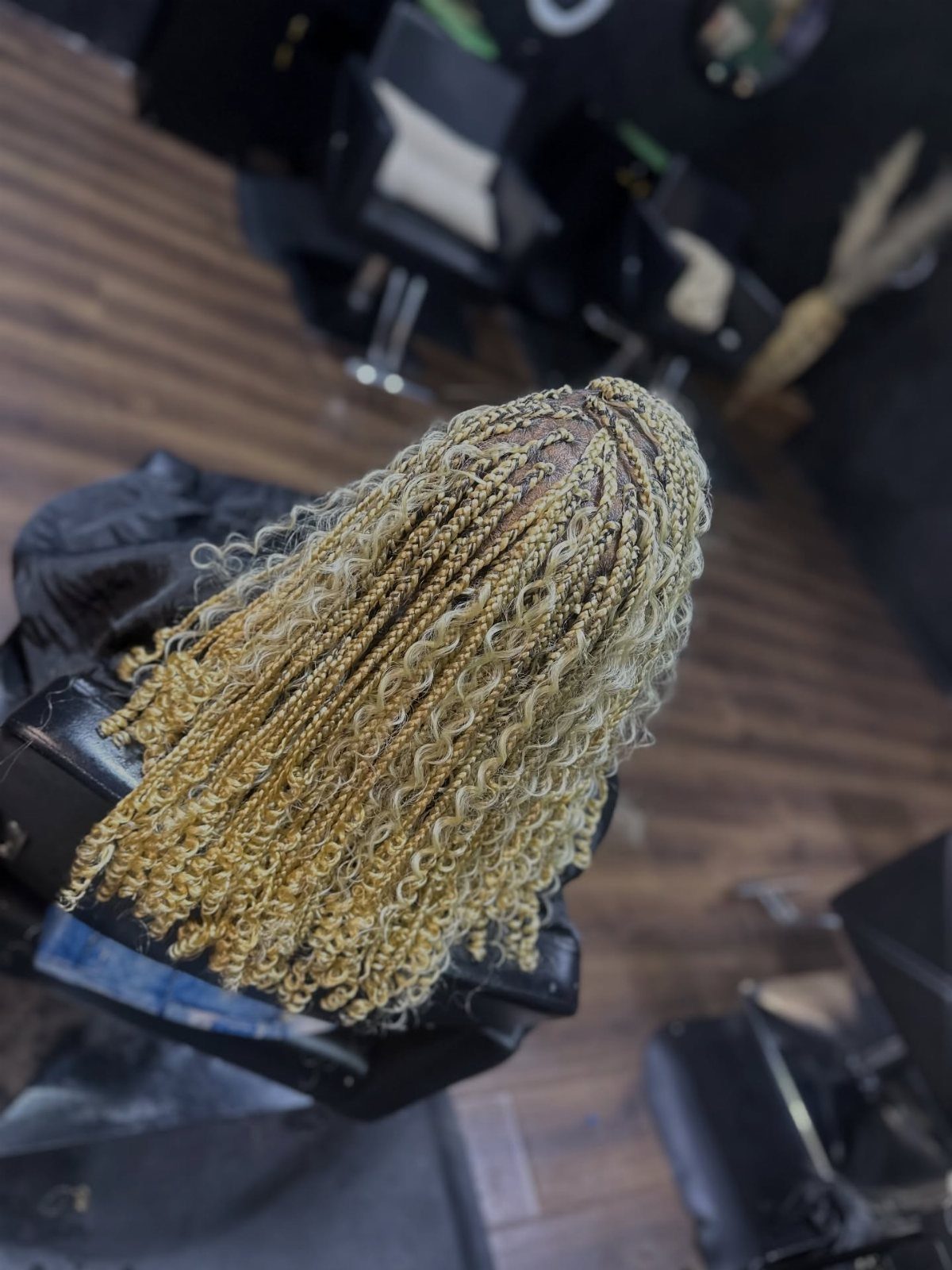 Honey-blonde braids with curly ends cascade down a seated person's back